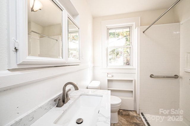 bathroom featuring toilet, vanity, and a tile shower