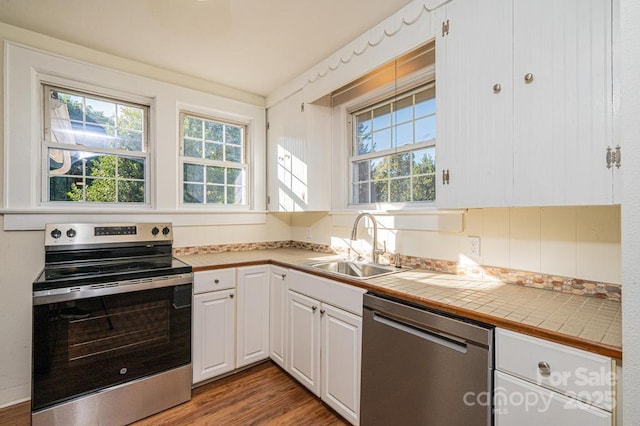 kitchen featuring appliances with stainless steel finishes, white cabinetry, sink, tile countertops, and hardwood / wood-style flooring