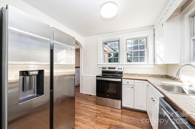 kitchen featuring light hardwood / wood-style flooring, appliances with stainless steel finishes, sink, white cabinetry, and tile counters