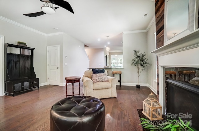 living room featuring a stone fireplace, crown molding, dark wood-type flooring, and ceiling fan