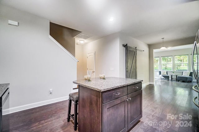 kitchen featuring a kitchen island, a barn door, dark hardwood / wood-style floors, dark brown cabinetry, and decorative light fixtures