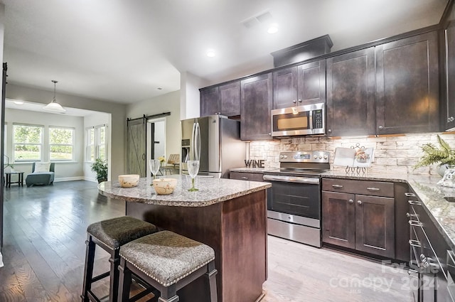 kitchen with light hardwood / wood-style flooring, stainless steel appliances, a barn door, dark brown cabinetry, and pendant lighting