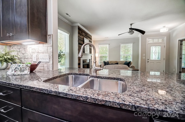 kitchen with sink, a large fireplace, stone countertops, dark brown cabinets, and crown molding