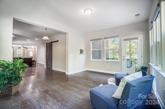 living room featuring a barn door, dark hardwood / wood-style floors, and ceiling fan