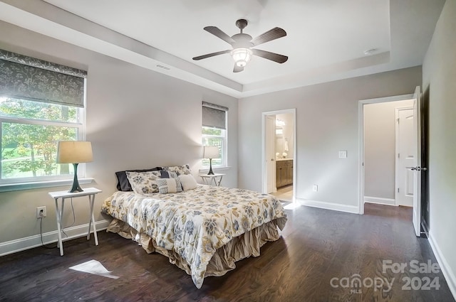 bedroom with ensuite bathroom, dark wood-type flooring, a raised ceiling, and ceiling fan