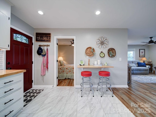 kitchen featuring a breakfast bar area, a ceiling fan, open floor plan, white cabinets, and butcher block countertops