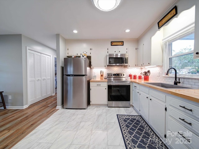 kitchen with stainless steel appliances, backsplash, a sink, and white cabinetry