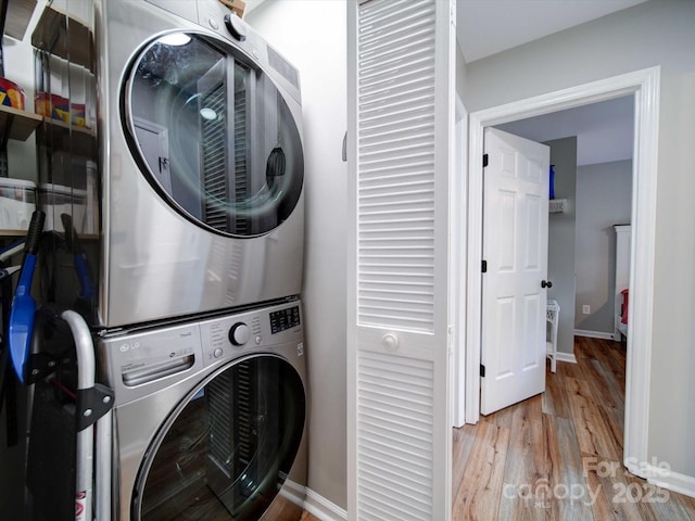 laundry area featuring stacked washing maching and dryer, light wood-style flooring, laundry area, and baseboards