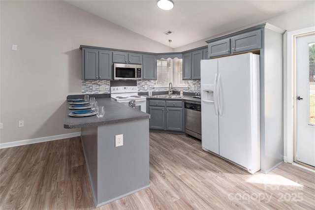 kitchen featuring kitchen peninsula, lofted ceiling, stainless steel appliances, sink, and tasteful backsplash