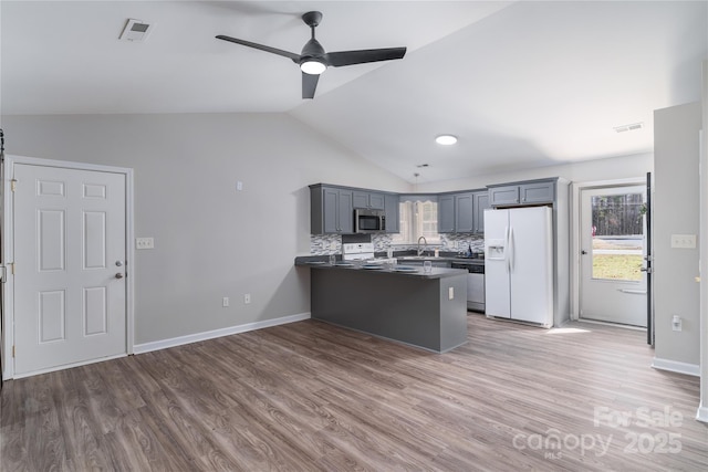 kitchen featuring white appliances, vaulted ceiling, backsplash, hardwood / wood-style floors, and kitchen peninsula