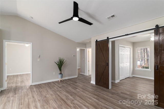 unfurnished bedroom with ceiling fan, vaulted ceiling, wood-type flooring, and a barn door