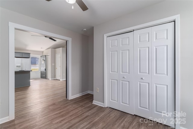 unfurnished bedroom featuring white refrigerator with ice dispenser, ceiling fan, a closet, and dark hardwood / wood-style floors