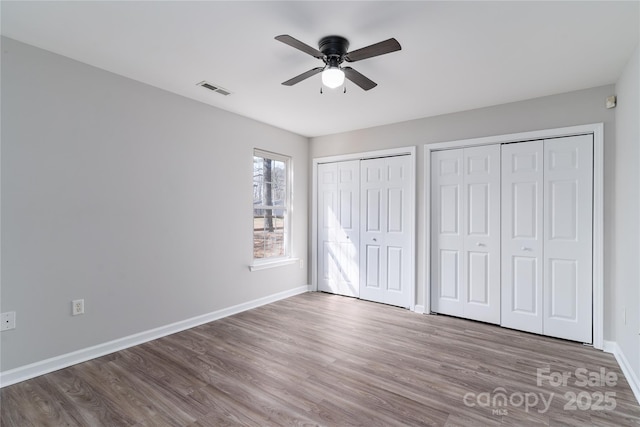 unfurnished bedroom with two closets, ceiling fan, and wood-type flooring