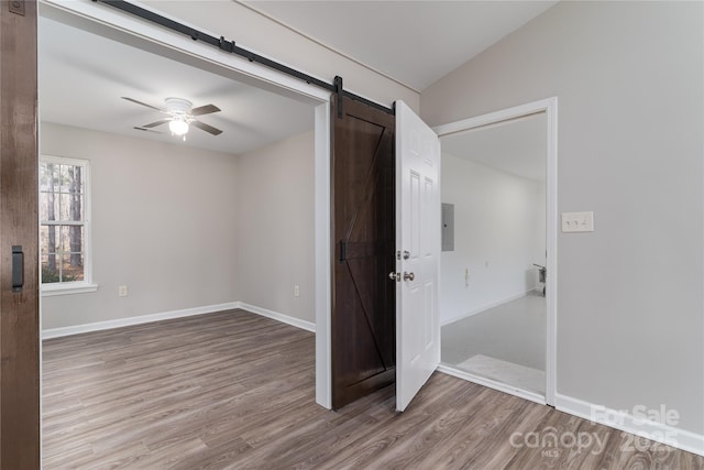 empty room with lofted ceiling, a barn door, electric panel, ceiling fan, and hardwood / wood-style floors