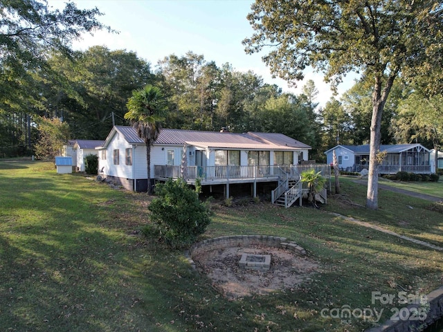 view of front of property featuring a deck, metal roof, an outdoor fire pit, stairs, and a front lawn