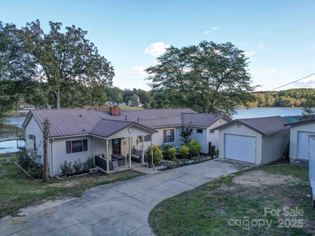 ranch-style house featuring a detached garage, a chimney, concrete driveway, a water view, and metal roof