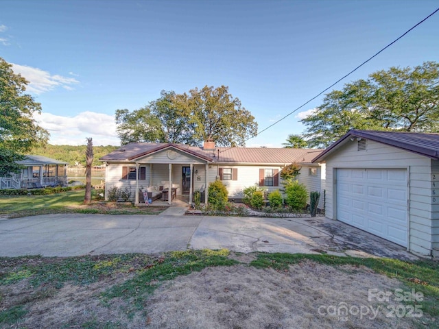 ranch-style house featuring covered porch, concrete driveway, a chimney, and metal roof