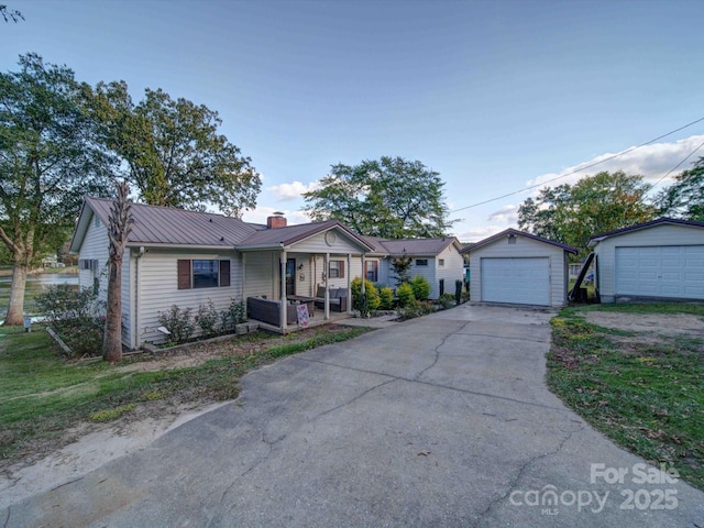 ranch-style home featuring driveway, a detached garage, a chimney, metal roof, and an outbuilding