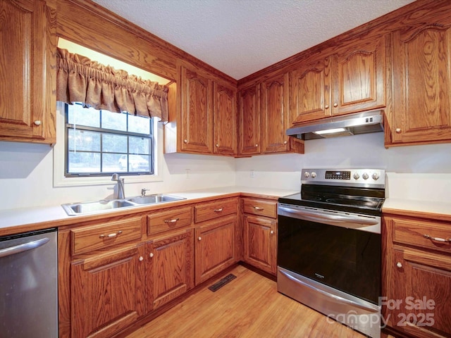 kitchen with under cabinet range hood, stainless steel appliances, a sink, light countertops, and brown cabinets