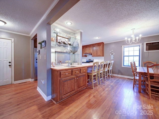 kitchen featuring light wood-style floors, light countertops, a wall mounted AC, brown cabinets, and crown molding