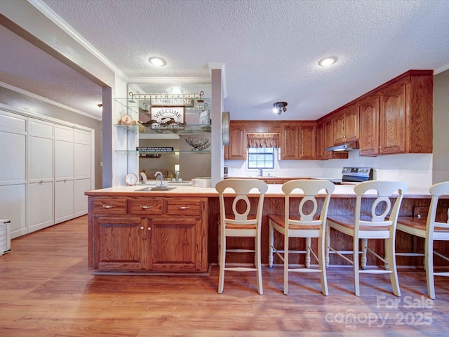 kitchen with brown cabinets, crown molding, light countertops, light wood-style flooring, and electric range