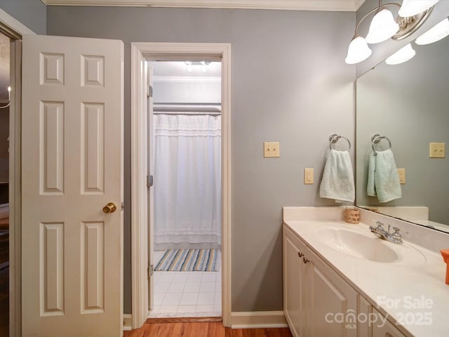 bathroom featuring baseboards, wood finished floors, crown molding, vanity, and a chandelier