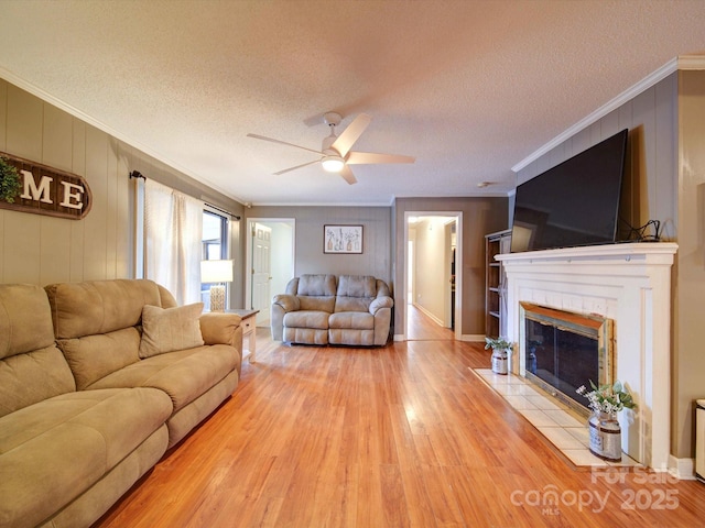 living room featuring light wood-style flooring, ornamental molding, a textured ceiling, and a tile fireplace