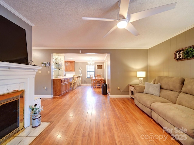 living area featuring a tile fireplace, ornamental molding, a textured ceiling, light wood-style floors, and ceiling fan with notable chandelier