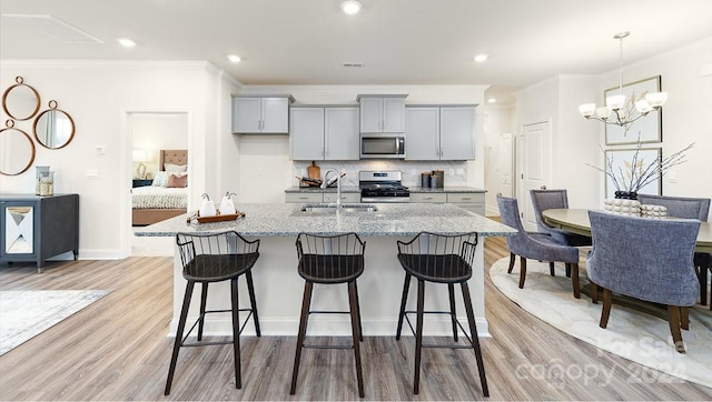 kitchen featuring tasteful backsplash, an island with sink, appliances with stainless steel finishes, light hardwood / wood-style flooring, and light stone counters