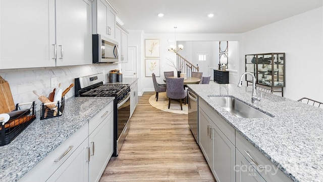 kitchen with light stone countertops, sink, light wood-type flooring, hanging light fixtures, and stainless steel appliances