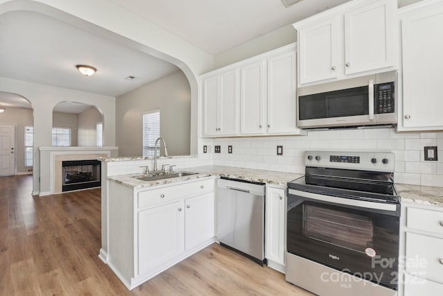 kitchen with light stone countertops, sink, kitchen peninsula, white cabinets, and appliances with stainless steel finishes