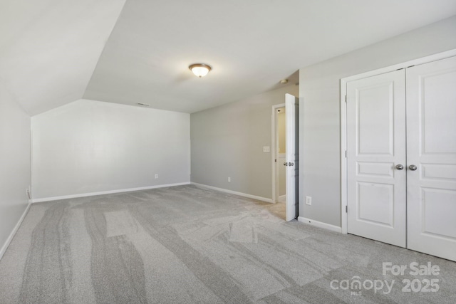 unfurnished bedroom with light carpet, a closet, and lofted ceiling