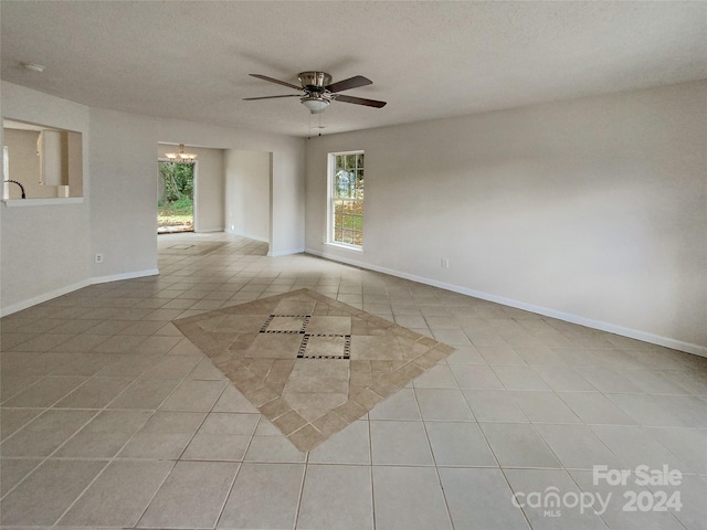 spare room with a textured ceiling, ceiling fan with notable chandelier, and light tile patterned floors