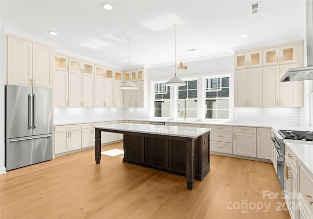 kitchen with high end appliances, crown molding, hanging light fixtures, and light wood-type flooring