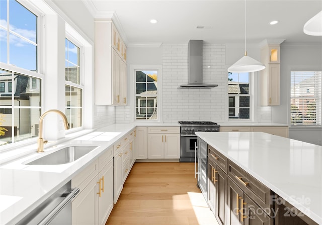 kitchen with wall chimney range hood, white cabinets, sink, and pendant lighting