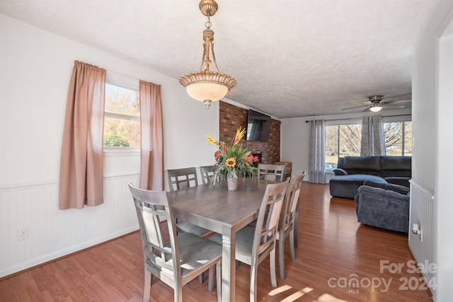 dining space with brick wall, hardwood / wood-style floors, a textured ceiling, a fireplace, and ceiling fan