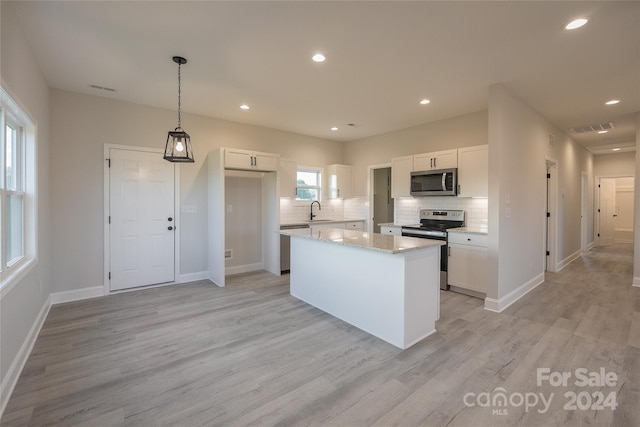 kitchen featuring a center island, white cabinets, hanging light fixtures, light wood-type flooring, and appliances with stainless steel finishes