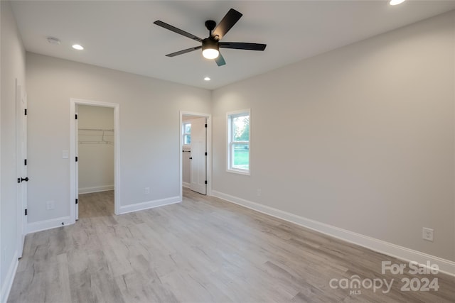 unfurnished bedroom featuring a walk in closet, ceiling fan, a closet, and light wood-type flooring