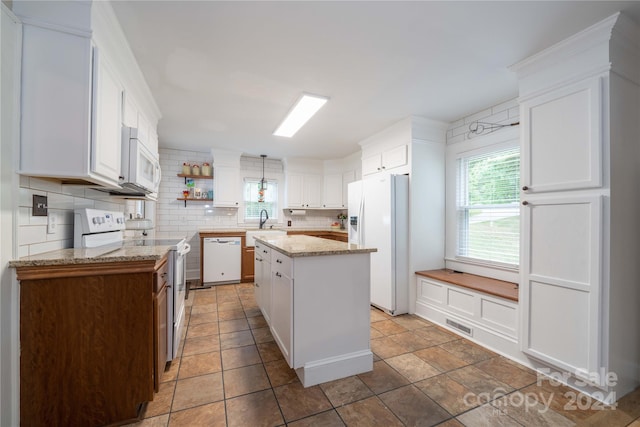 kitchen featuring white appliances, light stone countertops, backsplash, a center island, and white cabinetry