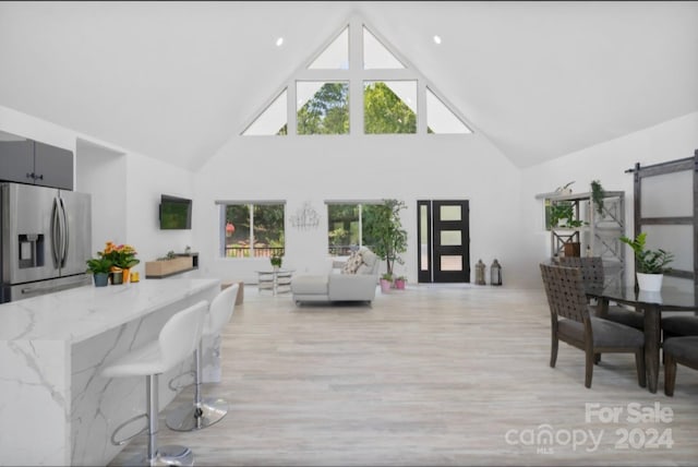 living room with high vaulted ceiling, a healthy amount of sunlight, light hardwood / wood-style flooring, and a barn door