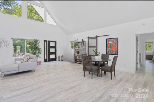 dining space featuring a healthy amount of sunlight, high vaulted ceiling, and a barn door