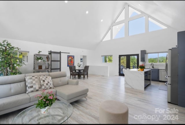 living room with light hardwood / wood-style flooring, high vaulted ceiling, sink, and a barn door