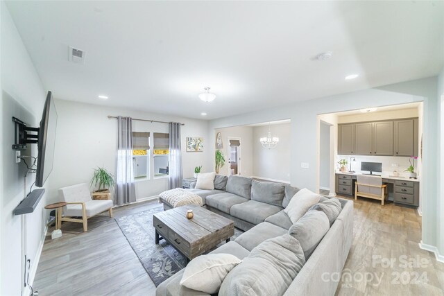 living room with built in desk, a chandelier, and light hardwood / wood-style flooring