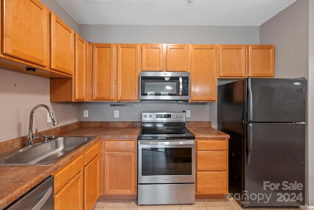 kitchen with a textured ceiling, appliances with stainless steel finishes, sink, and light tile patterned flooring