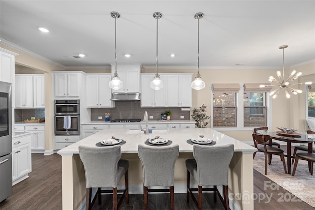 kitchen with hanging light fixtures, white cabinets, and a kitchen island with sink