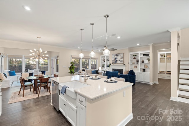 kitchen with decorative light fixtures, a center island with sink, stainless steel dishwasher, sink, and white cabinets