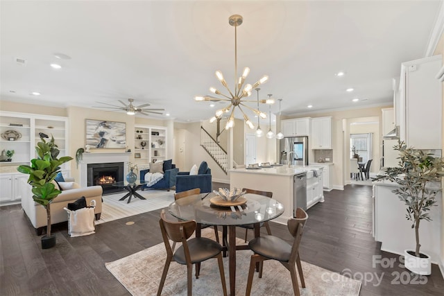 dining area with built in shelves, dark hardwood / wood-style floors, ceiling fan with notable chandelier, and ornamental molding