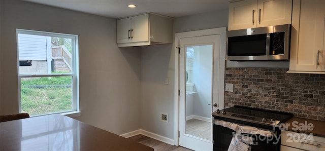 kitchen with black electric range oven, decorative backsplash, hardwood / wood-style flooring, and a healthy amount of sunlight