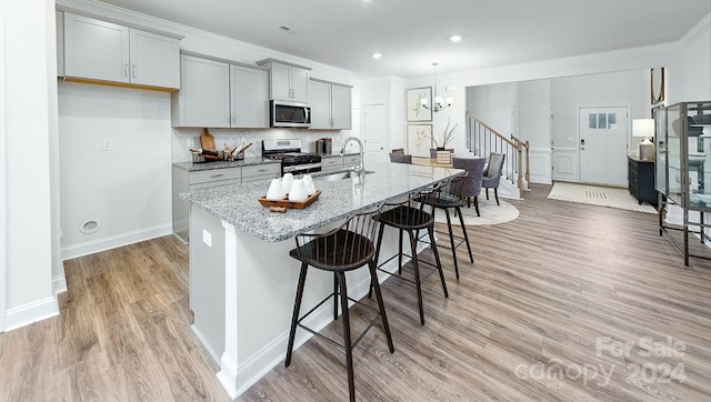 kitchen with an island with sink, sink, appliances with stainless steel finishes, light stone counters, and light hardwood / wood-style floors