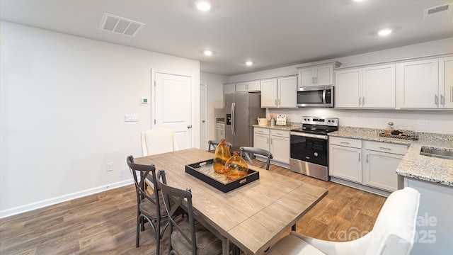 kitchen with stainless steel appliances, light stone countertops, sink, and wood-type flooring